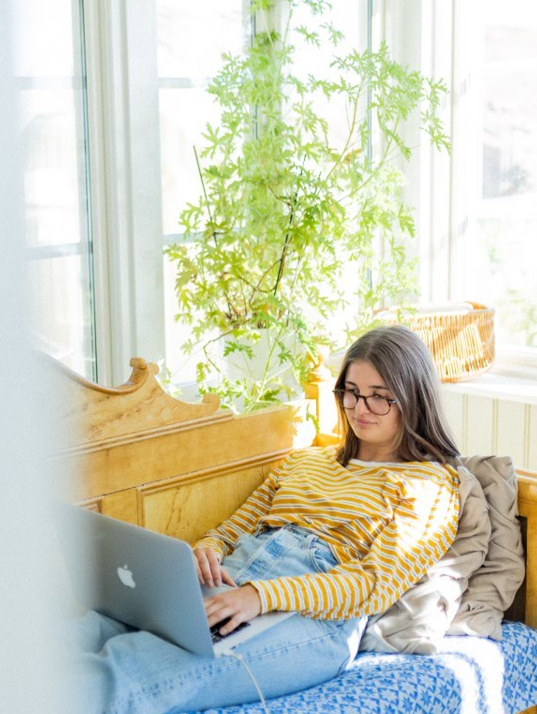 Flicka ligger på kökssoffa och surfar på sin laptop