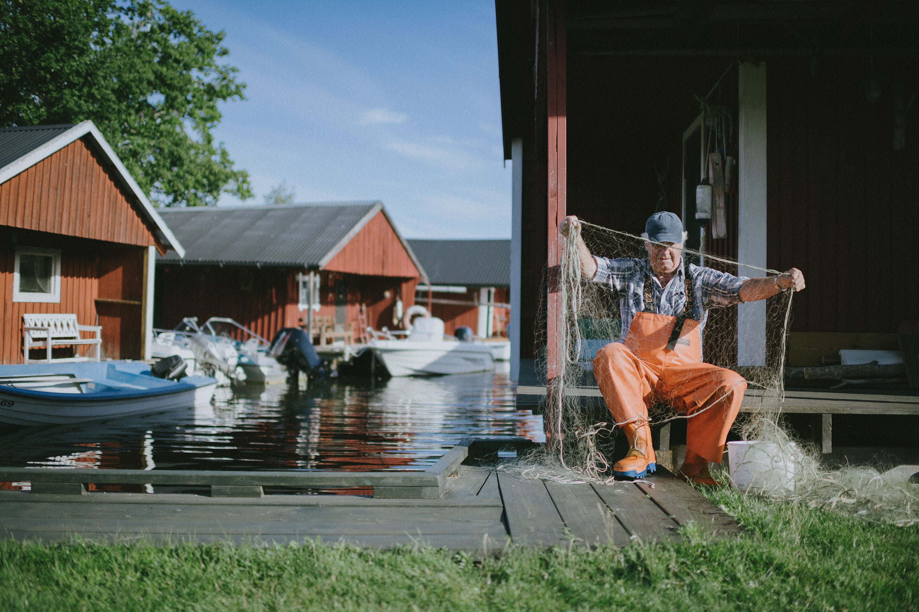 En äldre man ordnar med sina nät sittandes vid en liten fiskeby