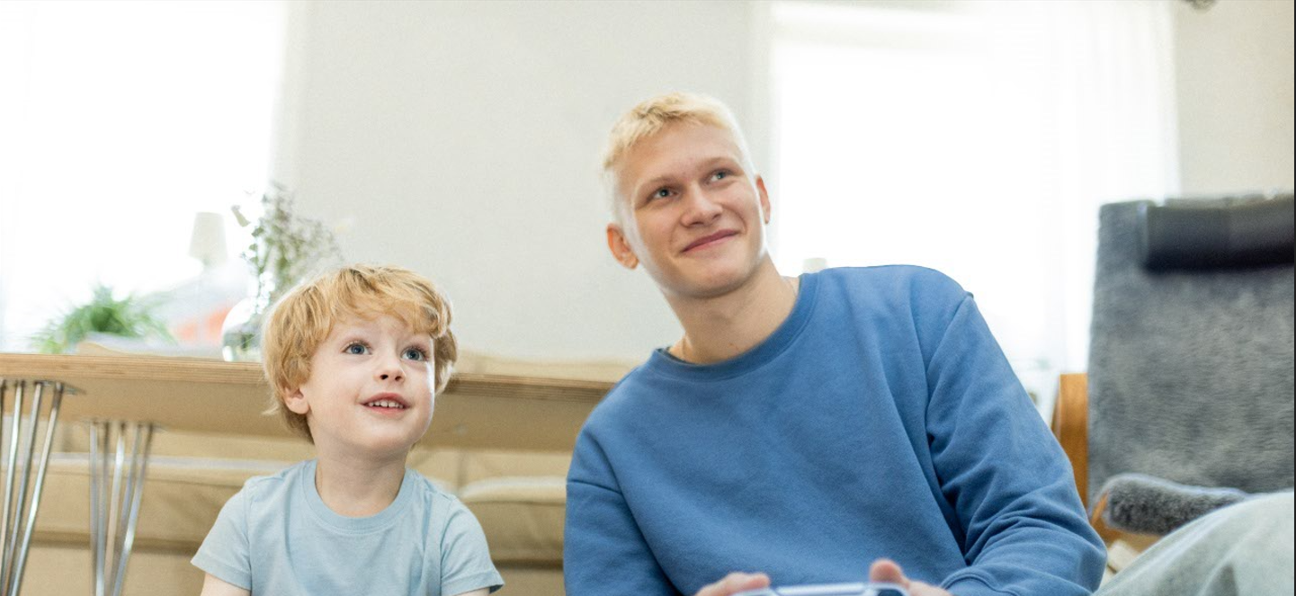 Barn och ung man spelar TV-spel sittandes på golvet.